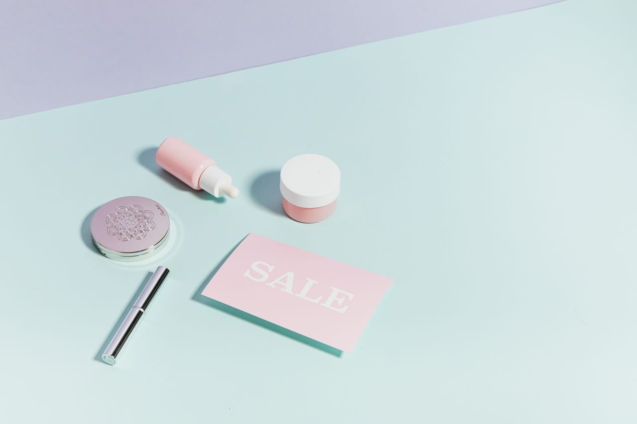 heros-img Clean flat lay of pastel pink beauty products and sale card on a light background.