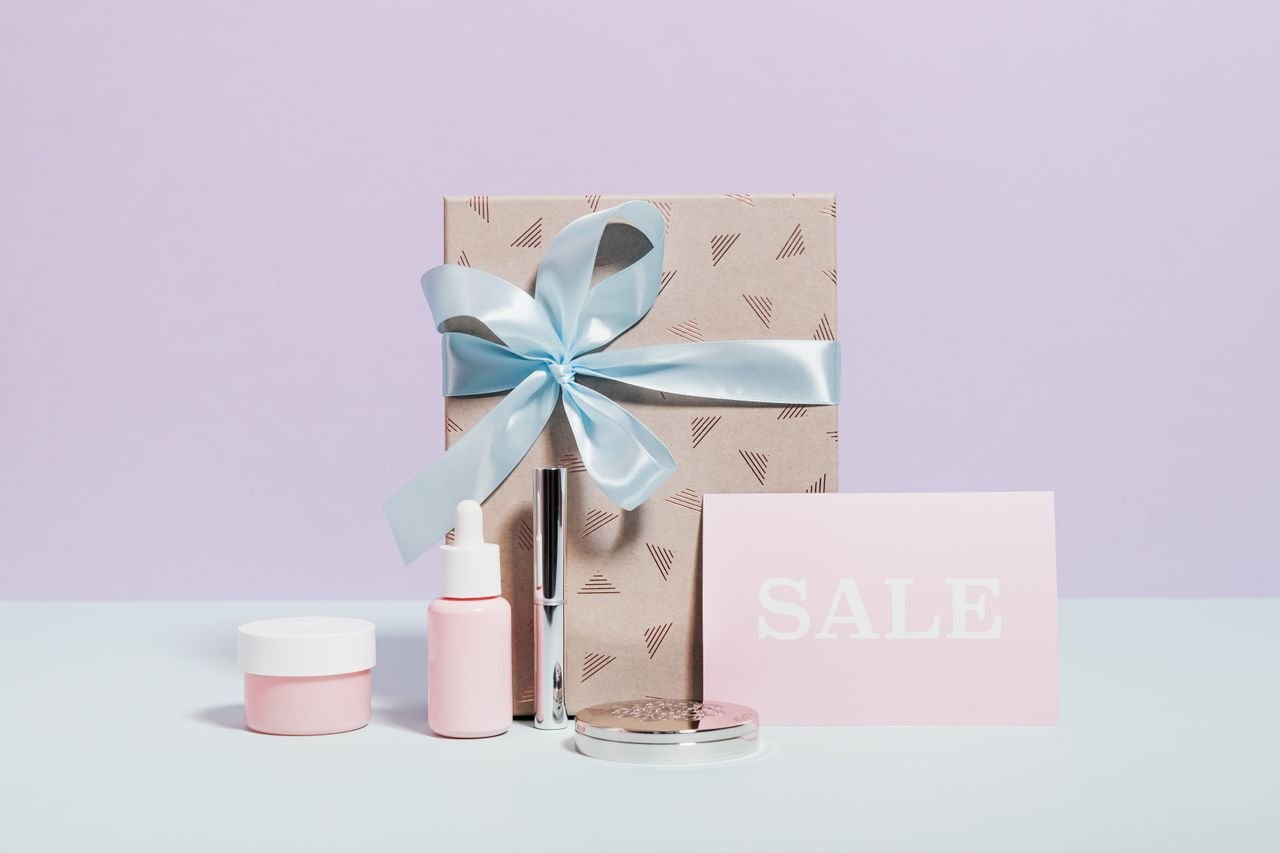 Stylish flat lay of beauty products and a gift with sale signage, perfect for promotions.